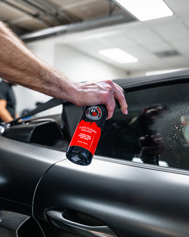 Detailer spraying HyperDrip Glass Cleaner on the window of a black sports car.