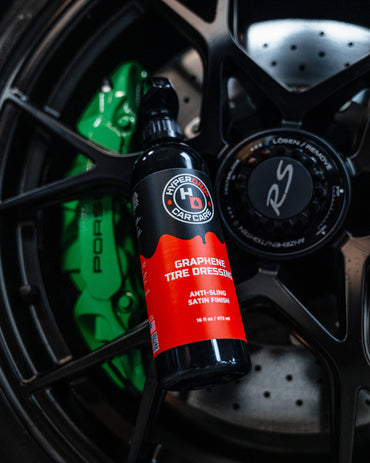 Close-up of HyperDrip Graphene Tire Dressing bottle placed against a Porsche wheel with green calipers.